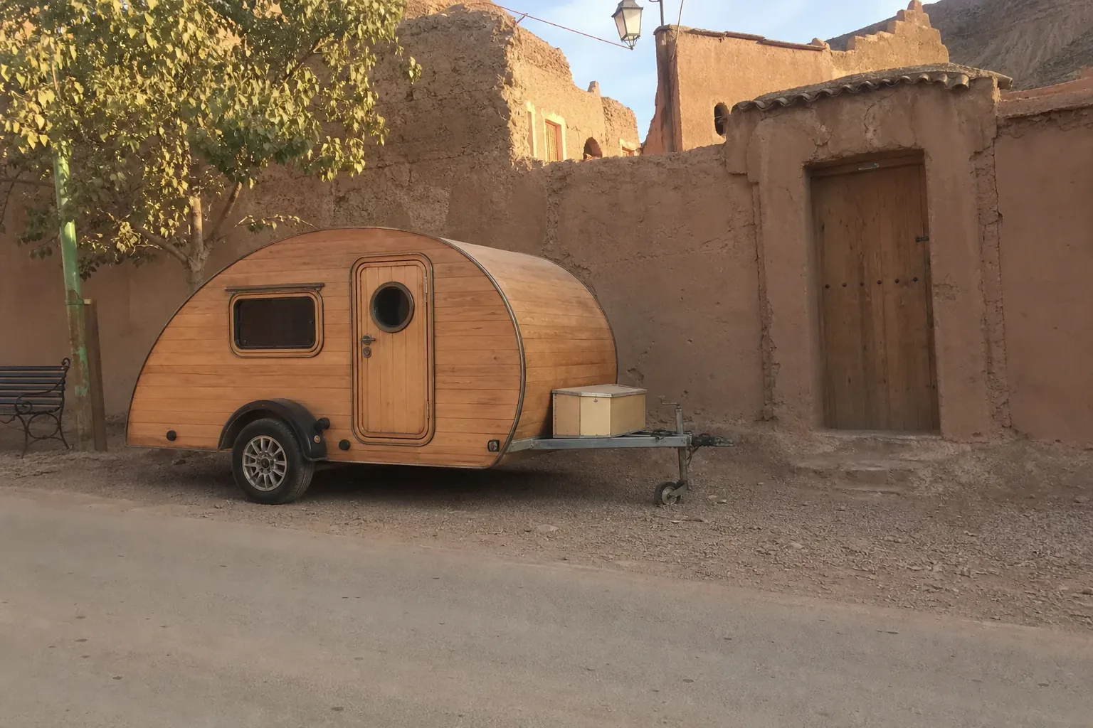 Caravane teardrop en bois clair garée dans une rue de village marocain, Anti-Atlas